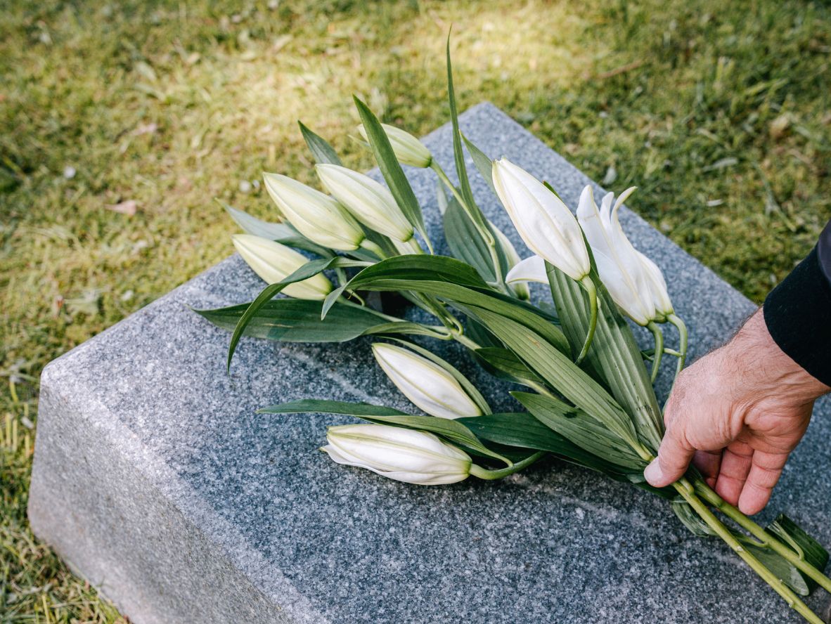 Emerson Monument Company image of a hand placing flowers on a granite marker in the cemetery