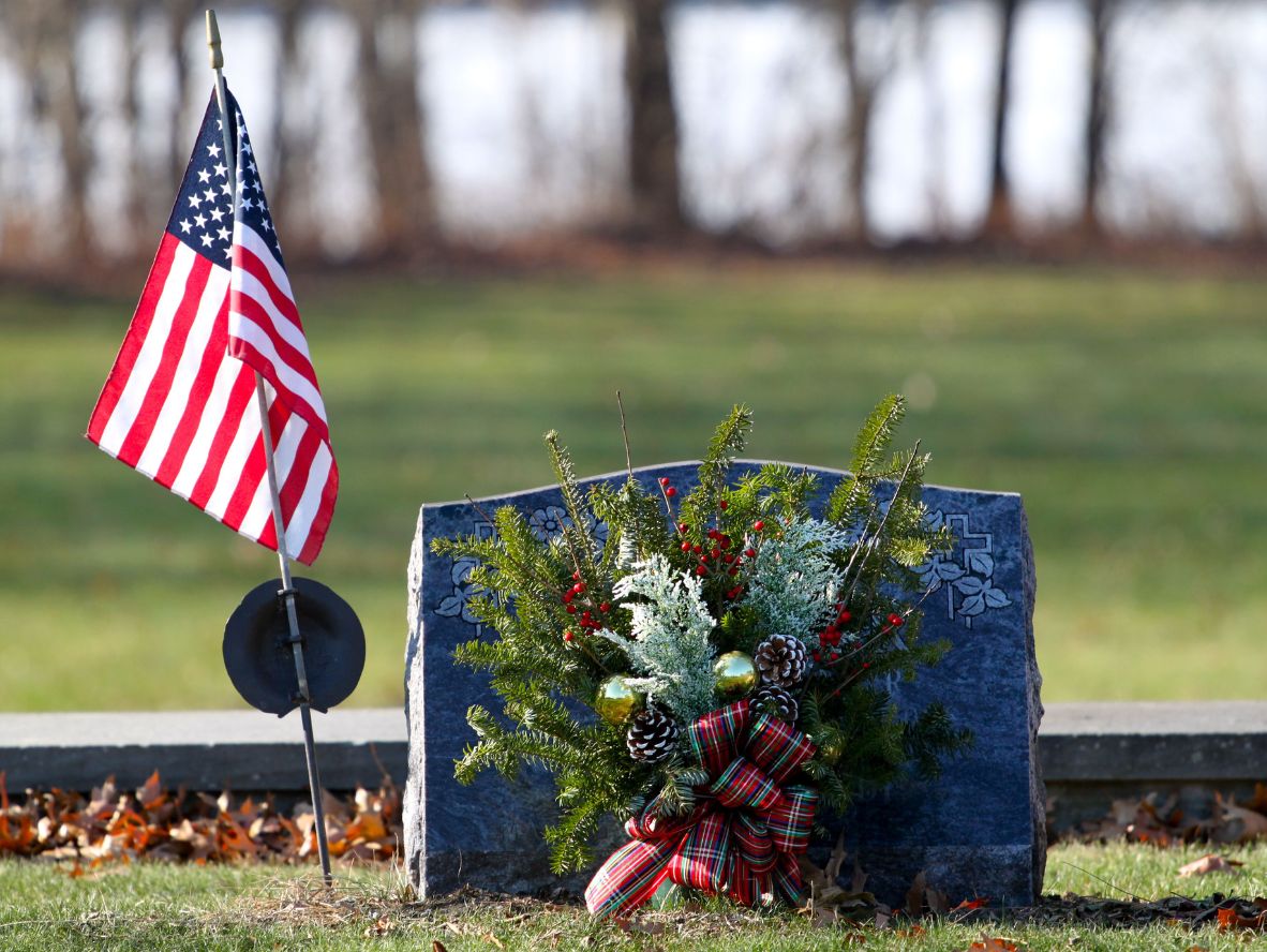 Emerson Monument Company image of a slant style memorial in the cemetery with floral decor and a US flag